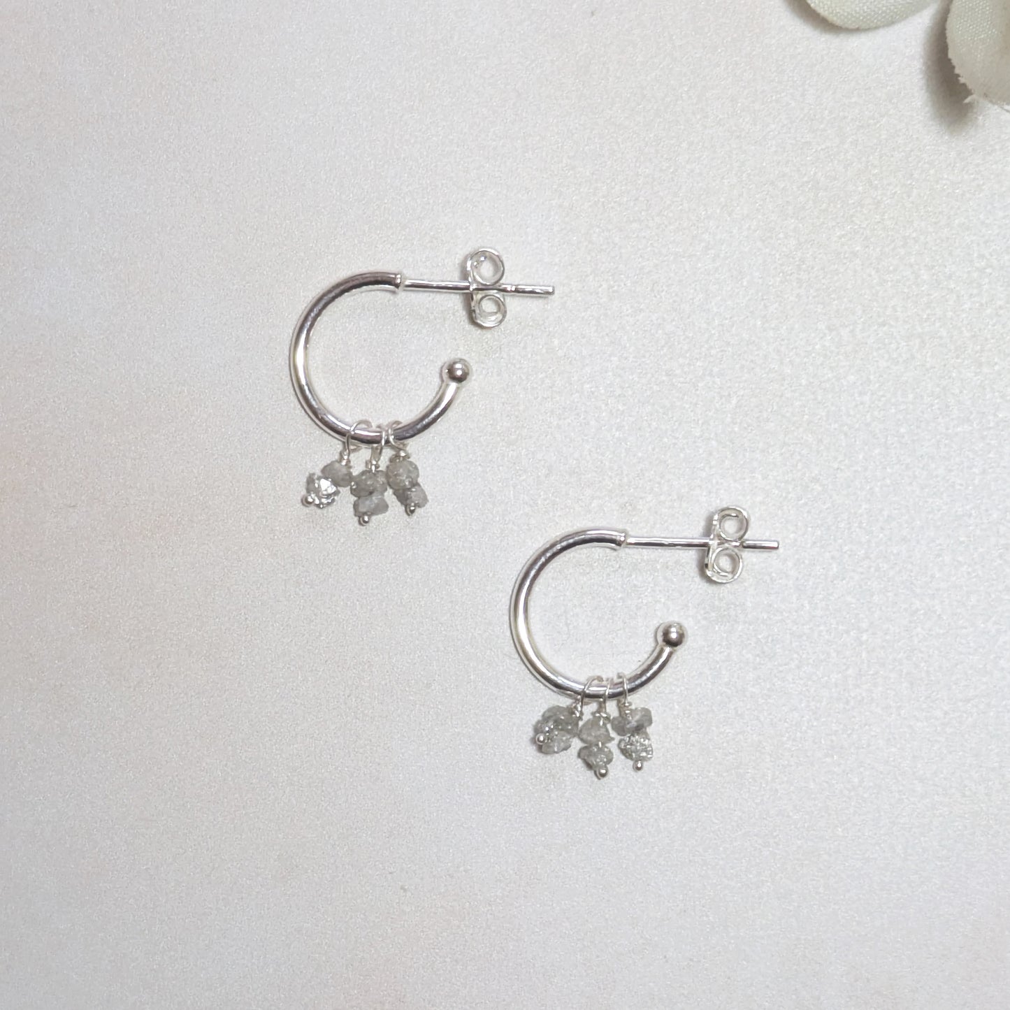 Silver hoop earrings with rough Diamond nugget dangling charms on a light grey background.