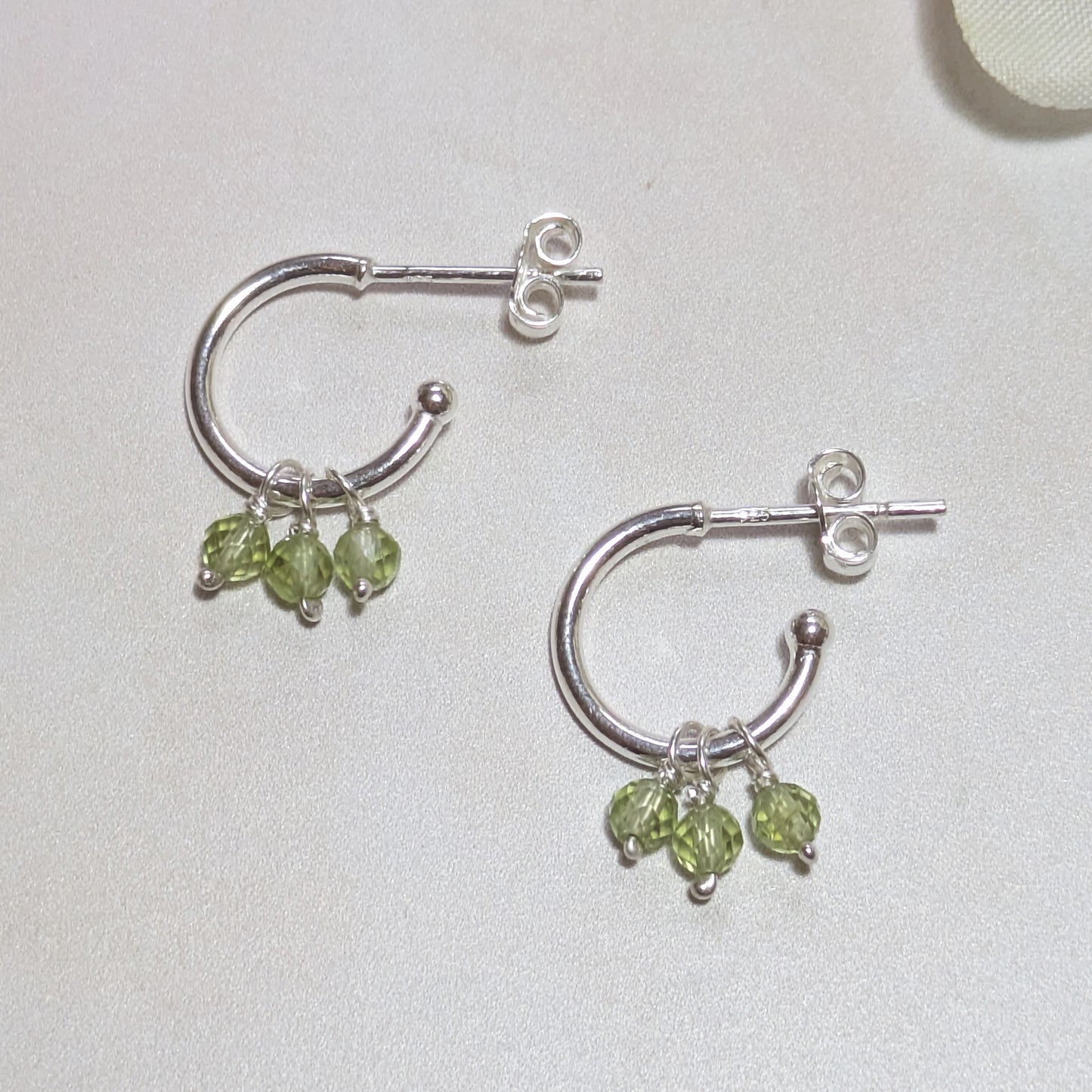 Silver hoop earrings with Peridot gemstone drops on a light background.