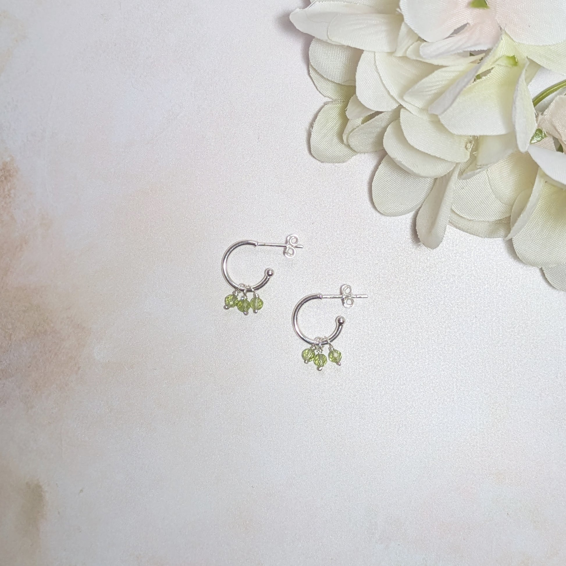 Silver hoop earrings with Peridot beads on a light background with flowers.
