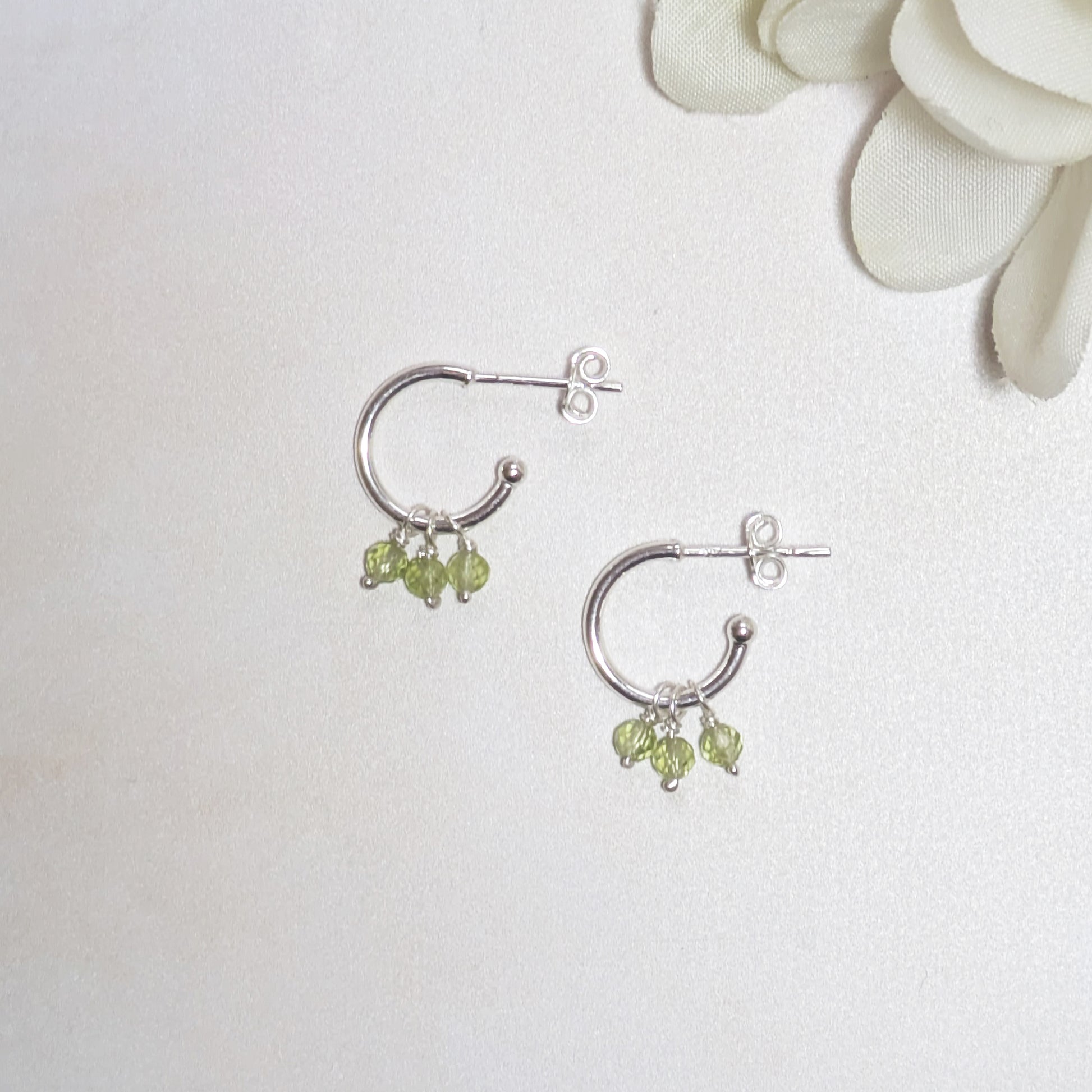 Silver hoop earrings with green Peridot beads on a white background.