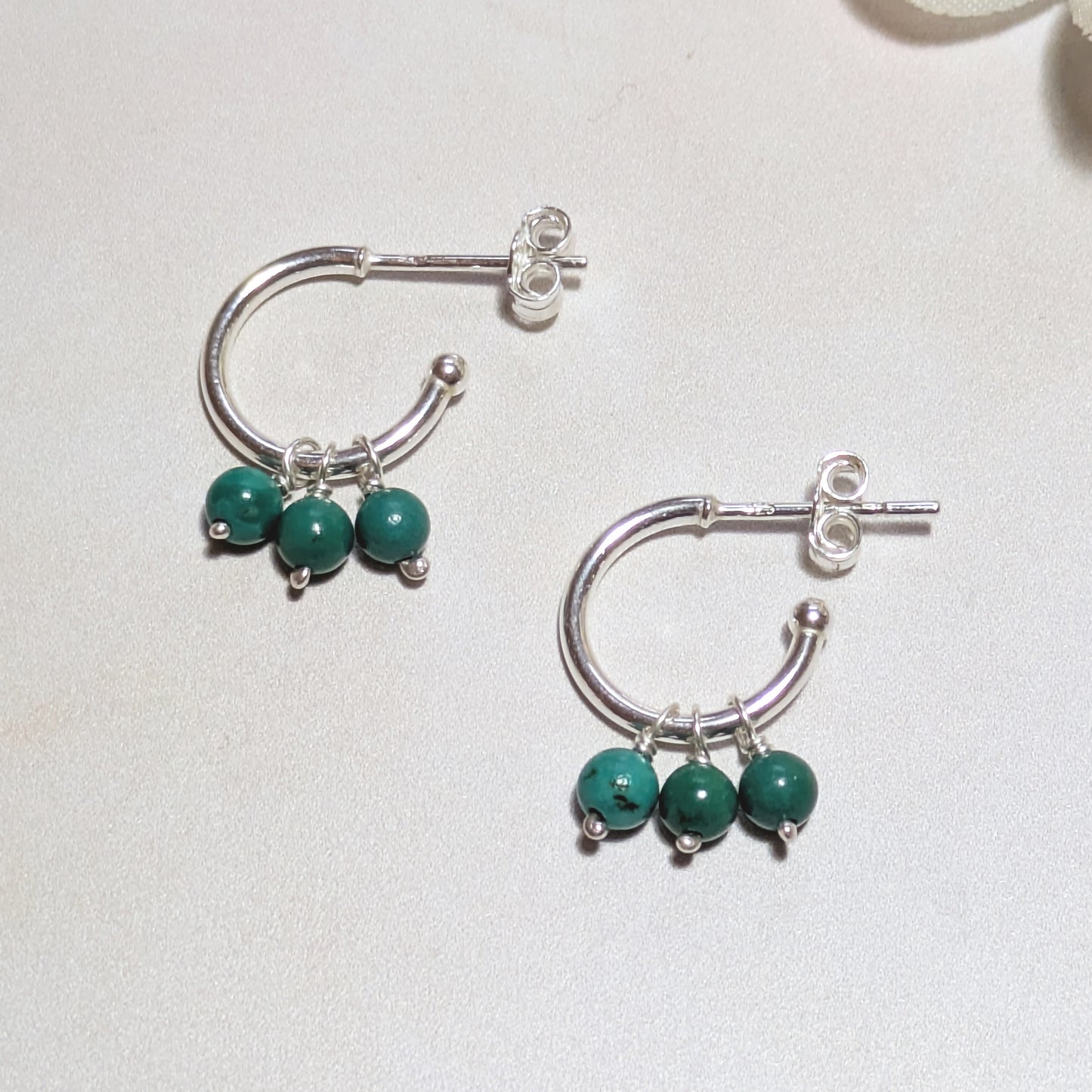 Silver hoop earrings with Turquoise gemstone beads on a light background.