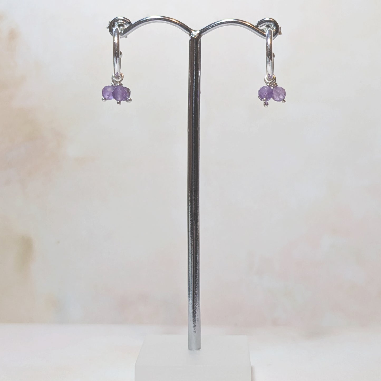 Pair of earrings with purple Amethyst gemstones on a silver stand against a white background.
