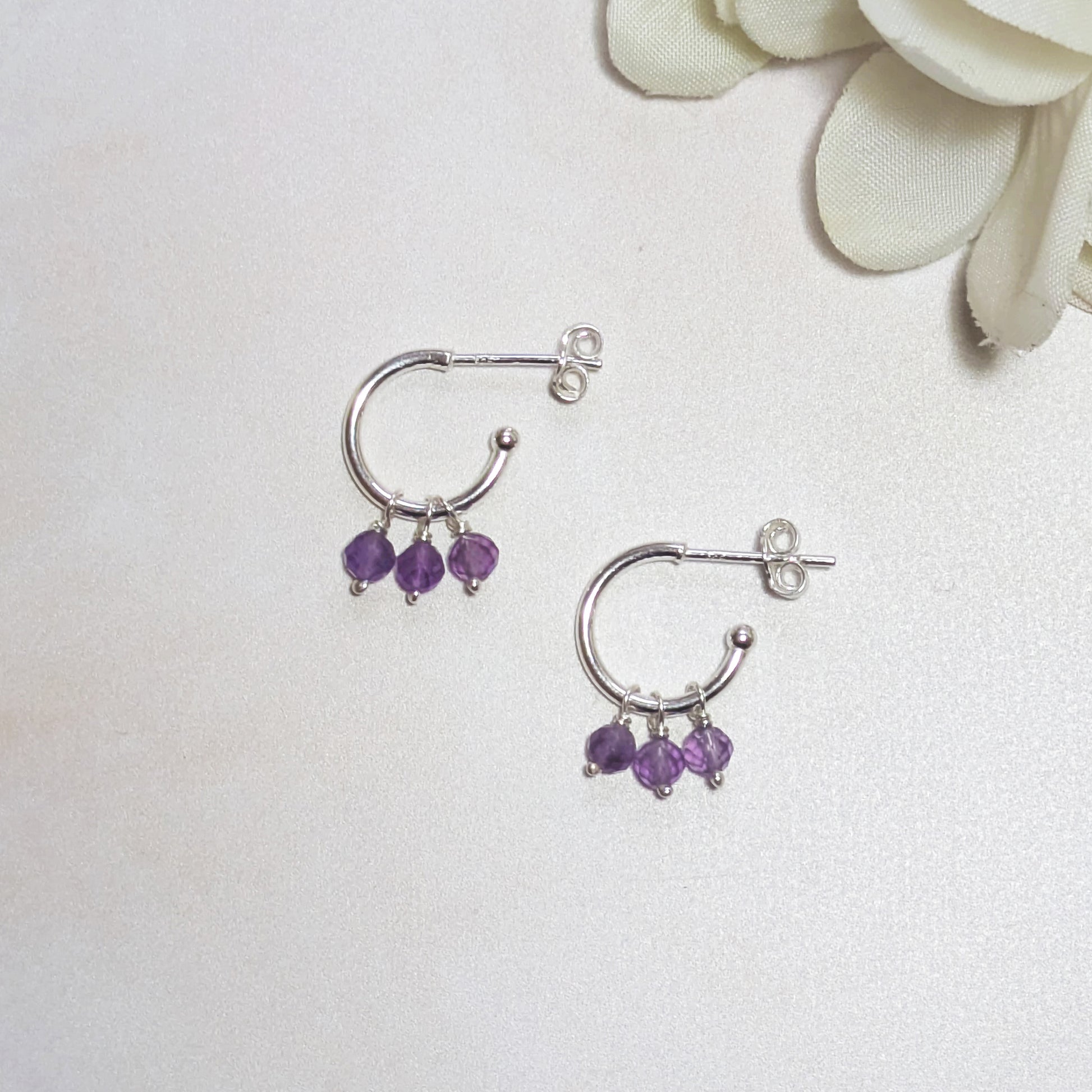 Silver hoop earrings with Amethyst gemstone beads on a white background.