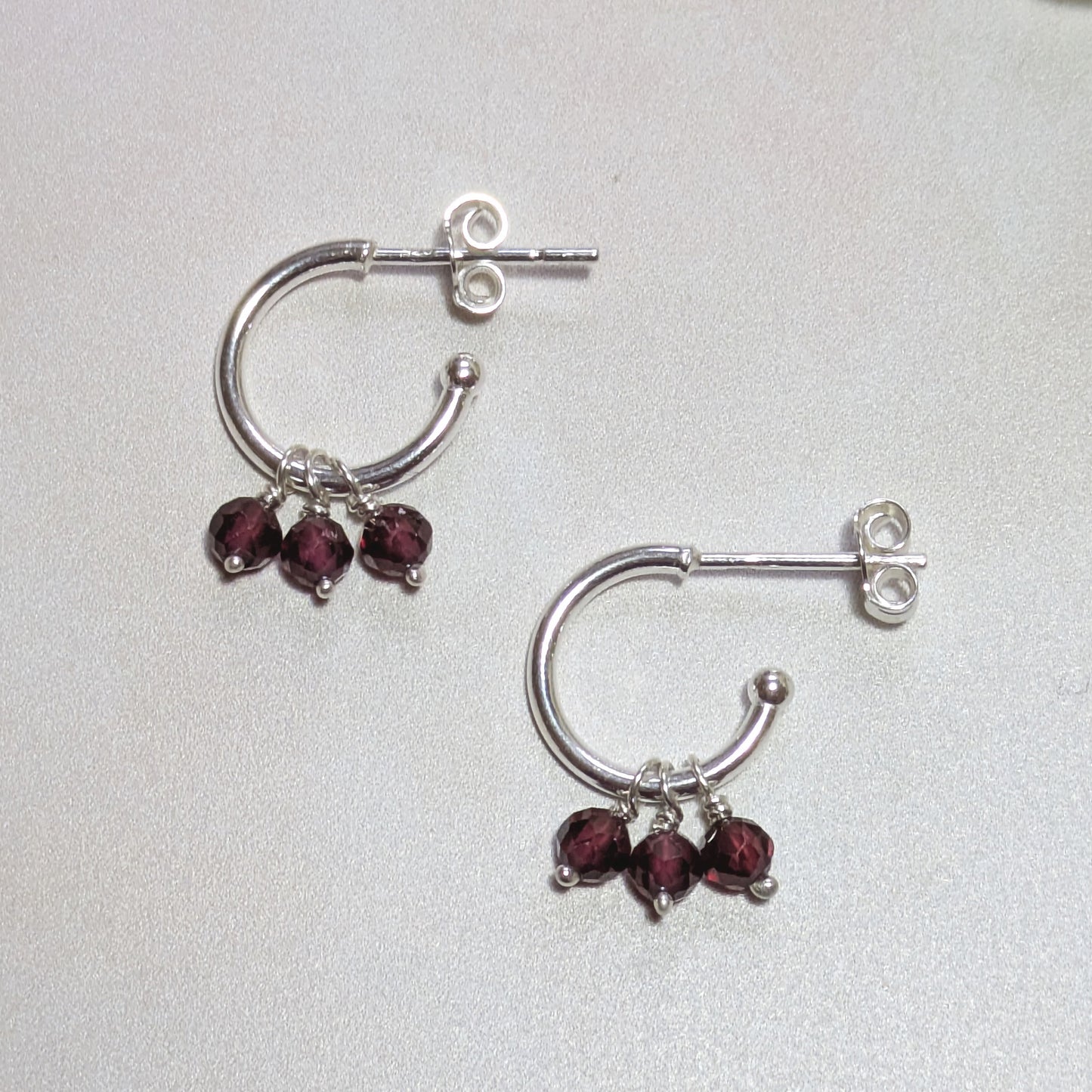 Silver hoop earrings with Garnet gemstones on a light grey background.