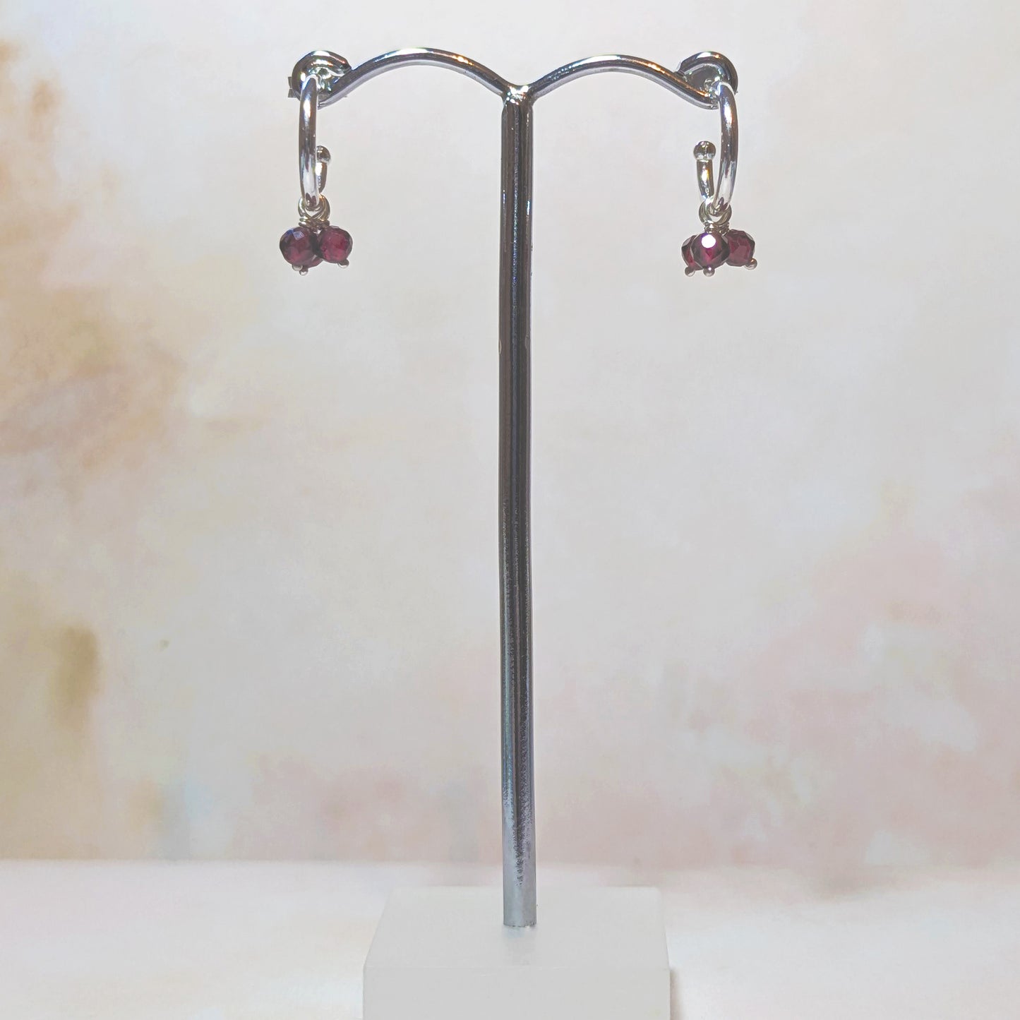 Silver hoop earrings with Garnet gemstones on a stand against a light background.