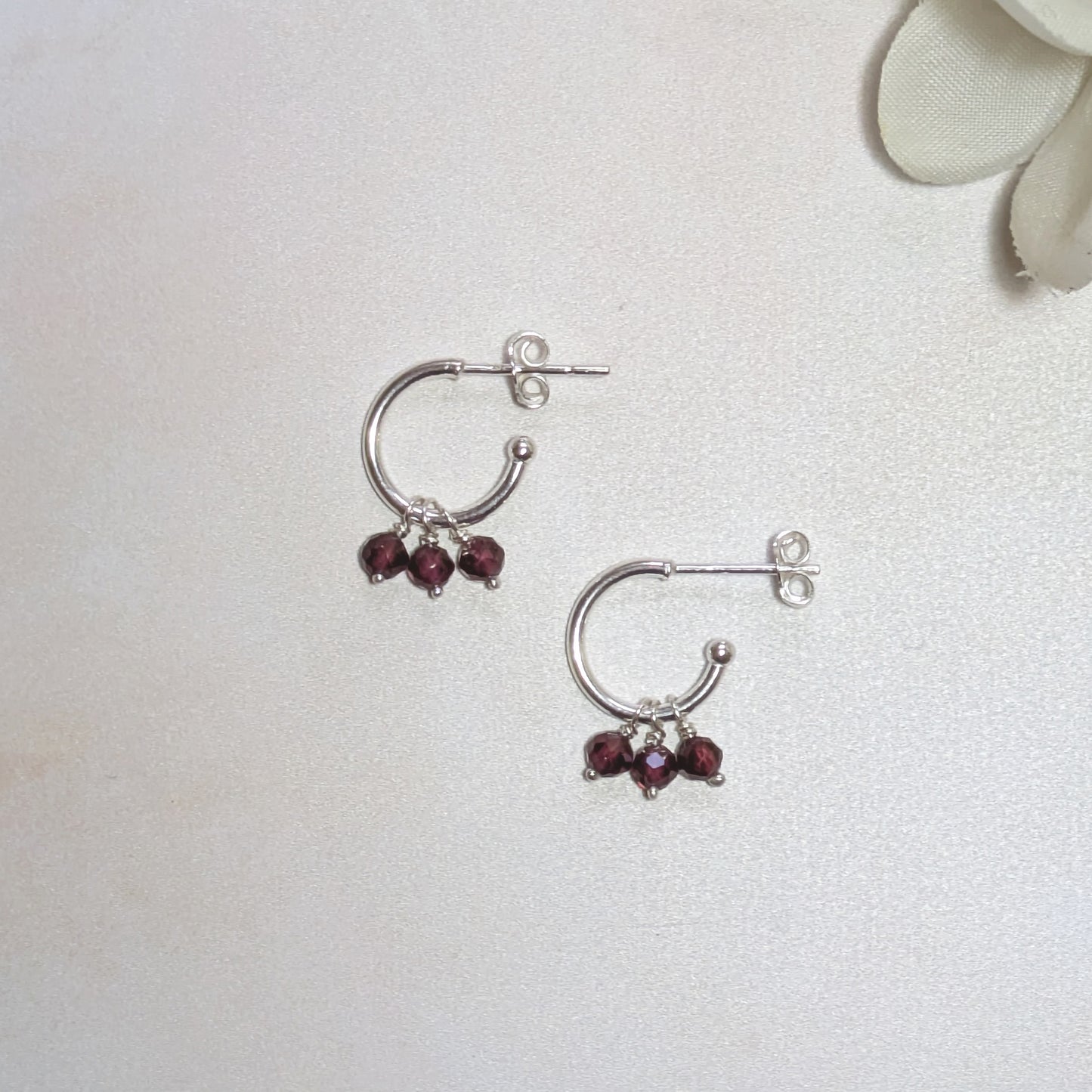 Silver hoop earrings with red gemstones on a light grey background.