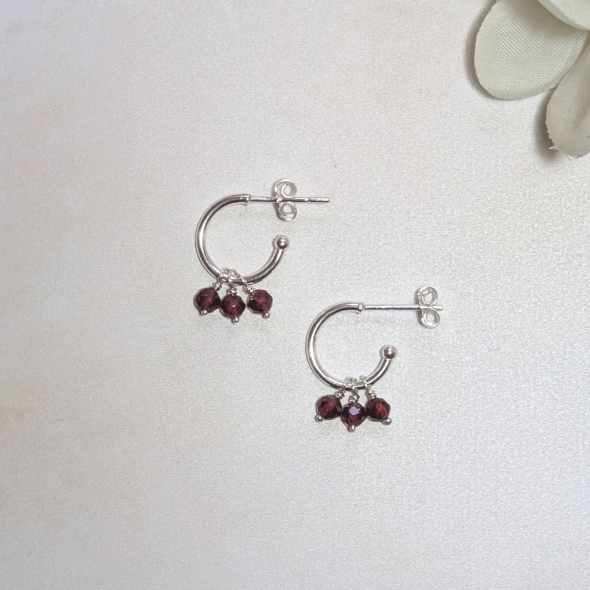 Silver hoop earrings with red gemstones on a light grey background.
