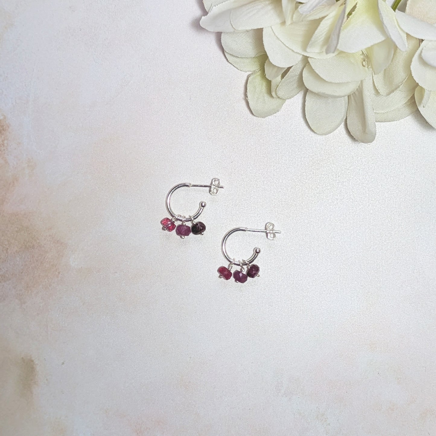 Silver hoop earrings with Rubies on a light background with white flowers.