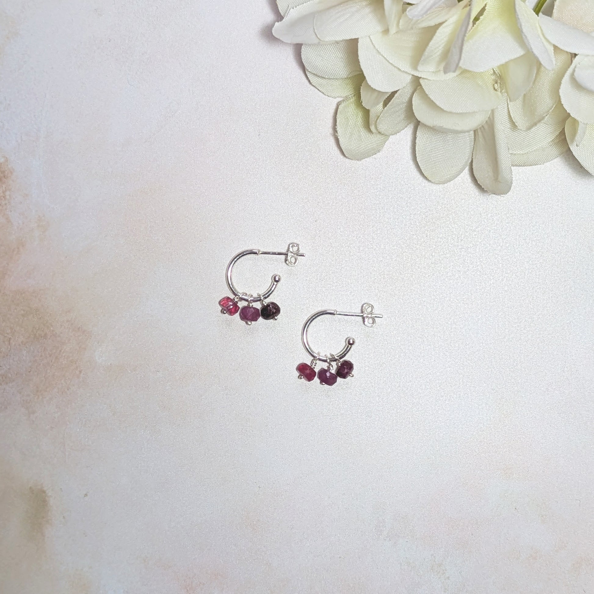 Silver hoop earrings with Rubies on a light background with white flowers.