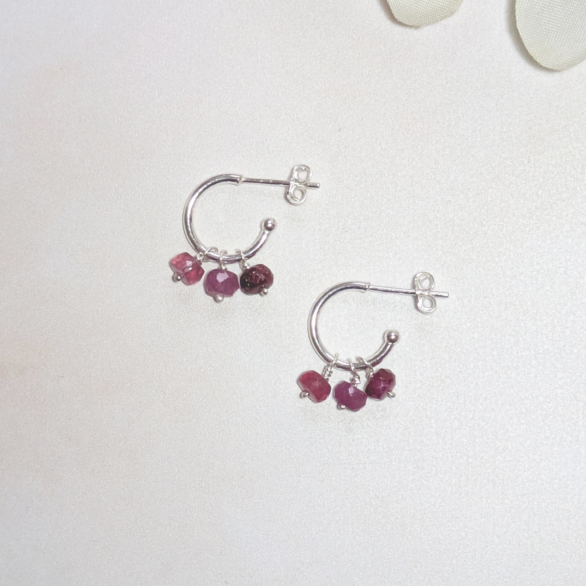 Silver hoop earrings with Ruby gemstones on a white background.