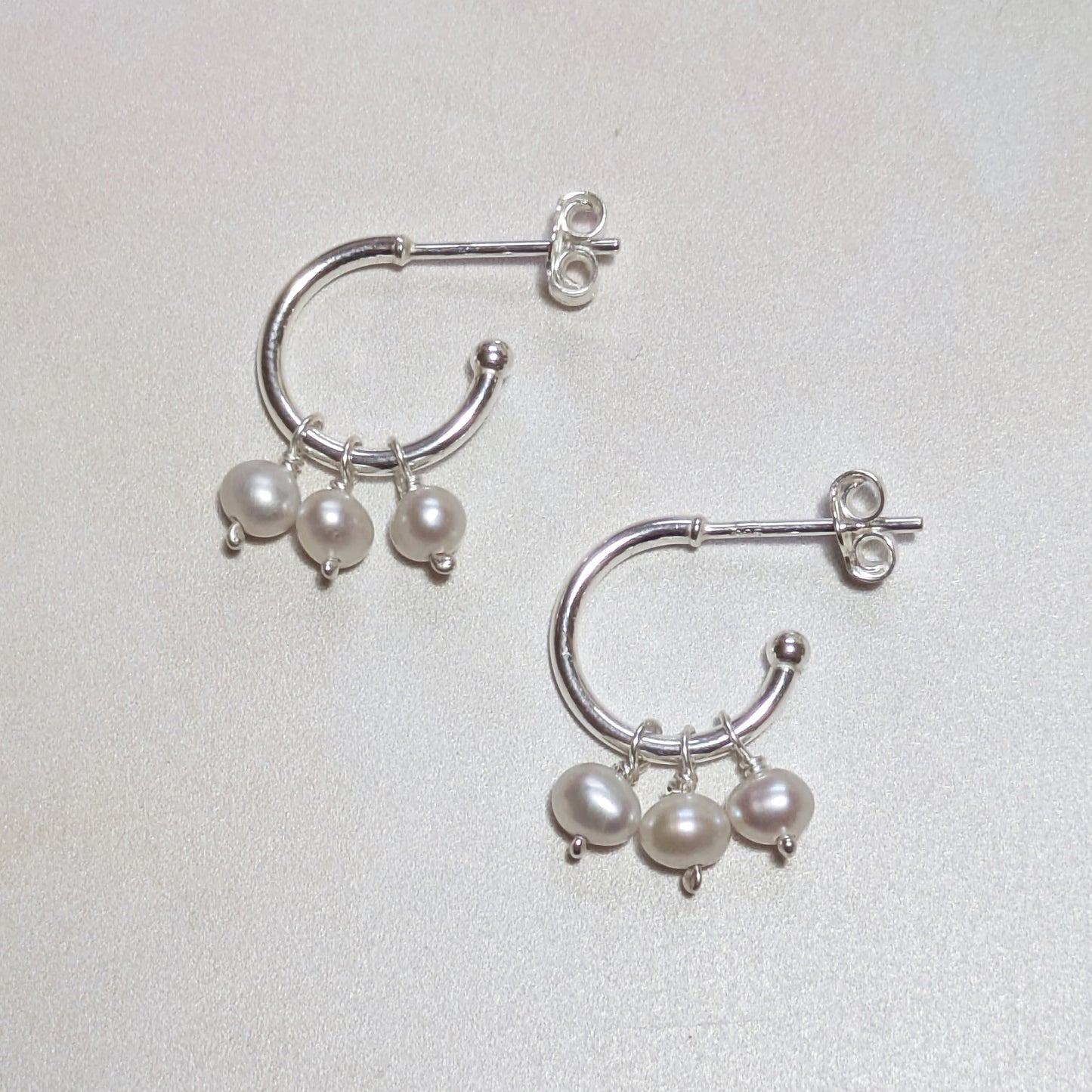 Silver hoop earrings with pearl drops on a light background.