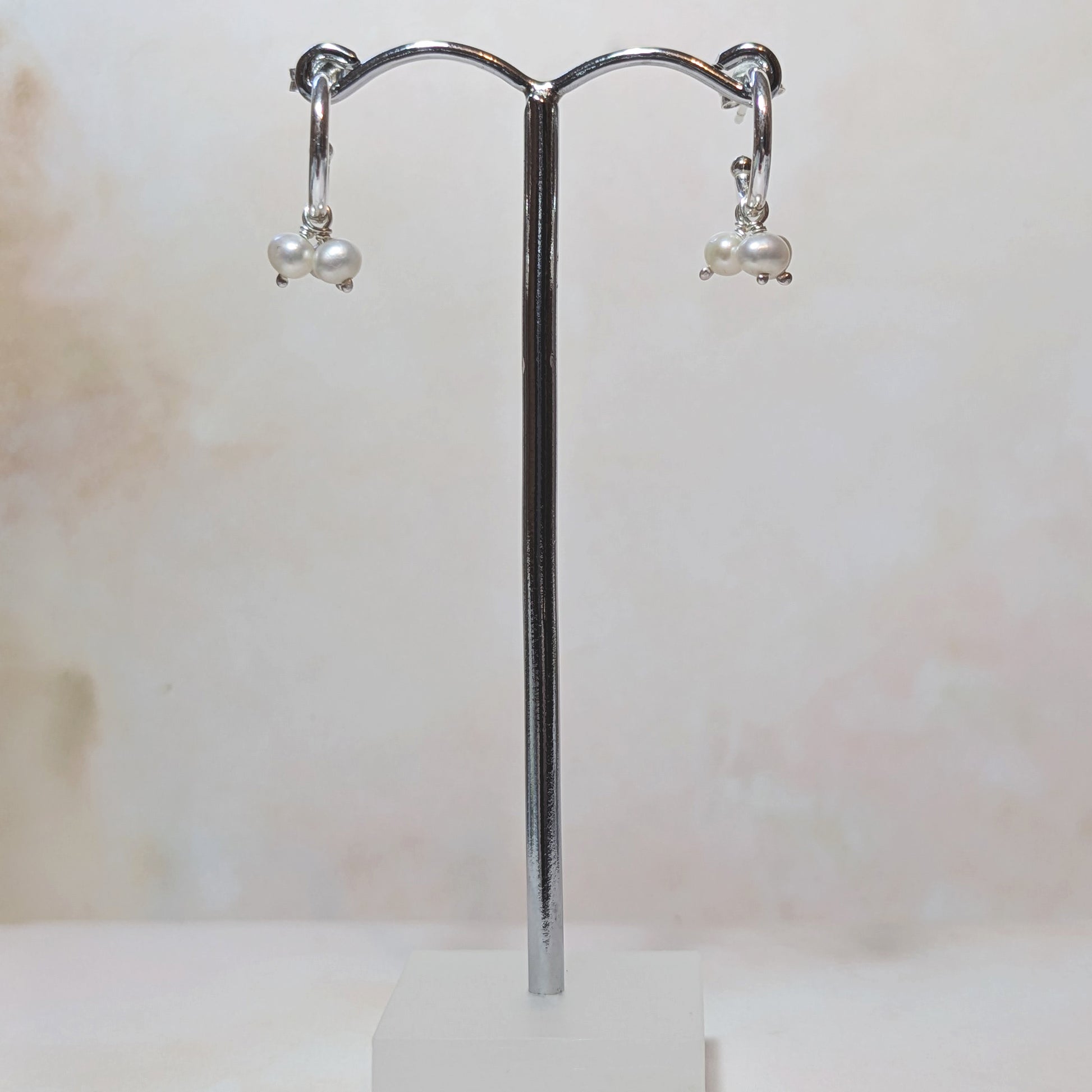 Pearl hoop earrings on a chrome stand against a neutral background.