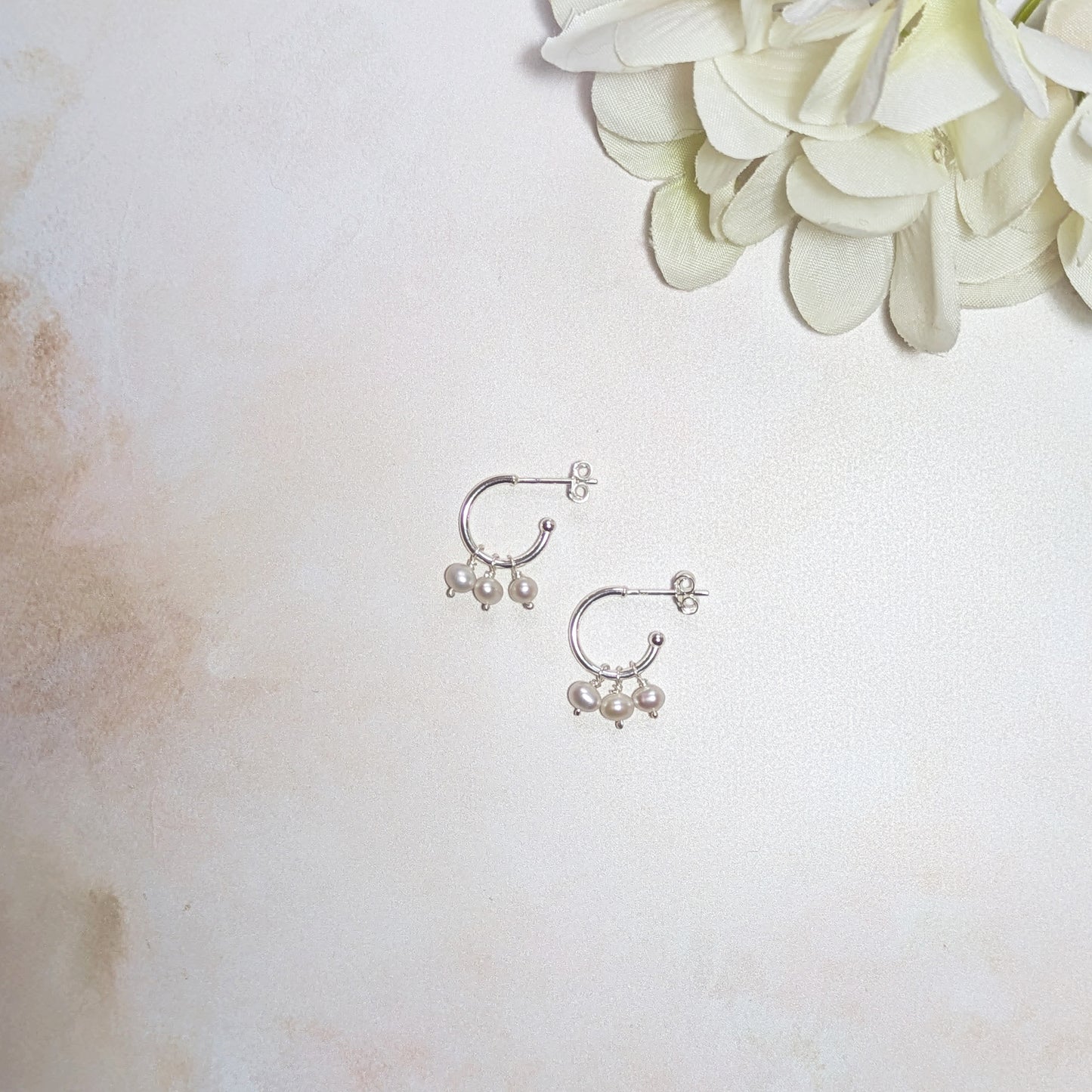 Silver hoop earrings with pearls charms on a light background with white flowers.