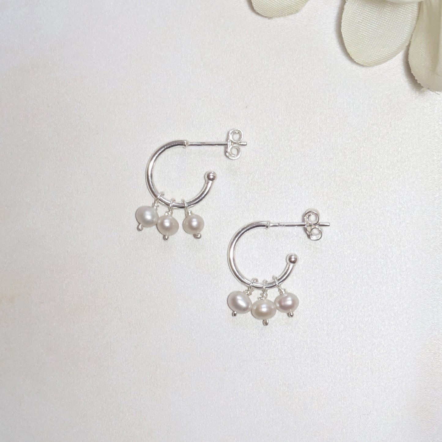 Silver hoop earrings with pearls on a light background.