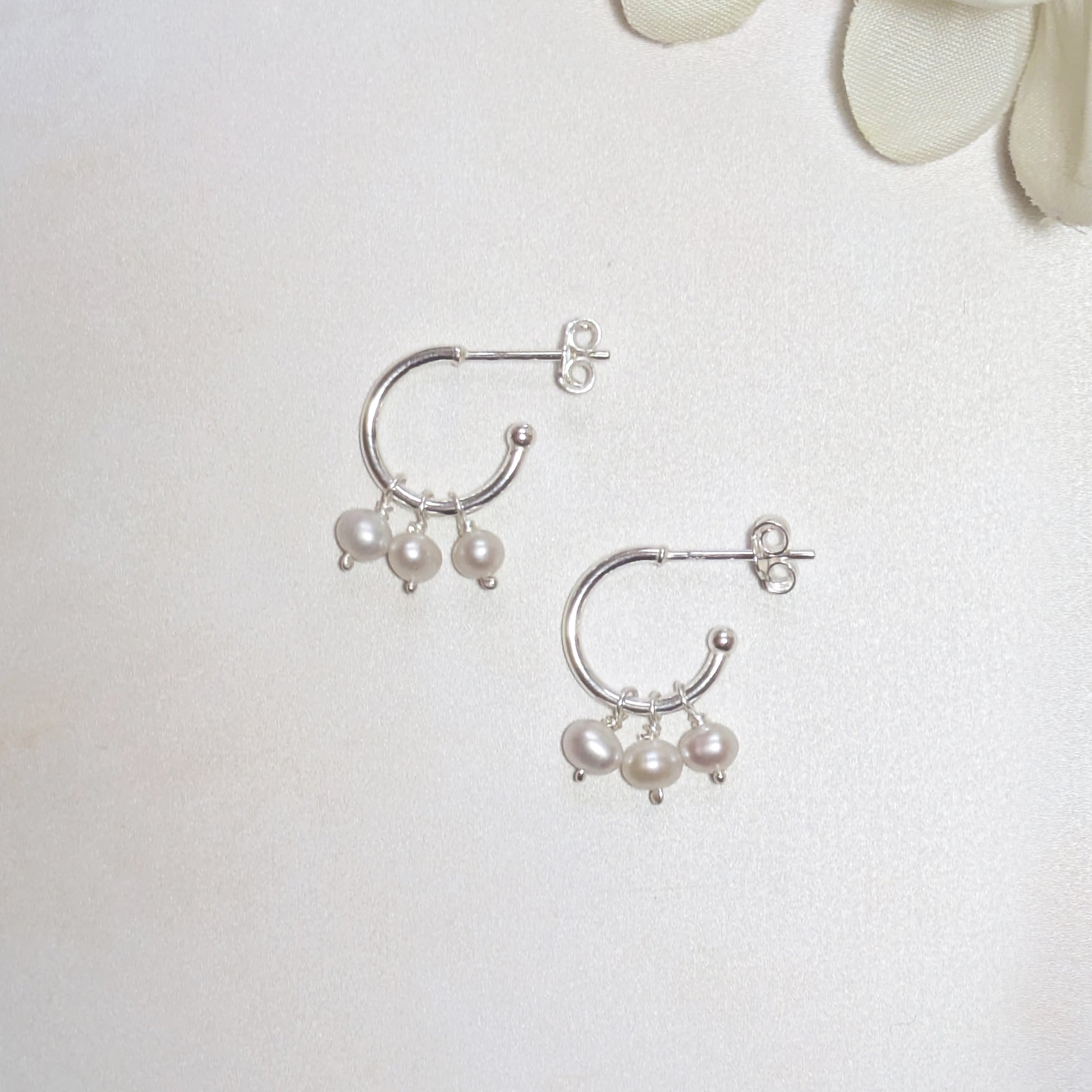 Silver hoop earrings with pearls on a light background.