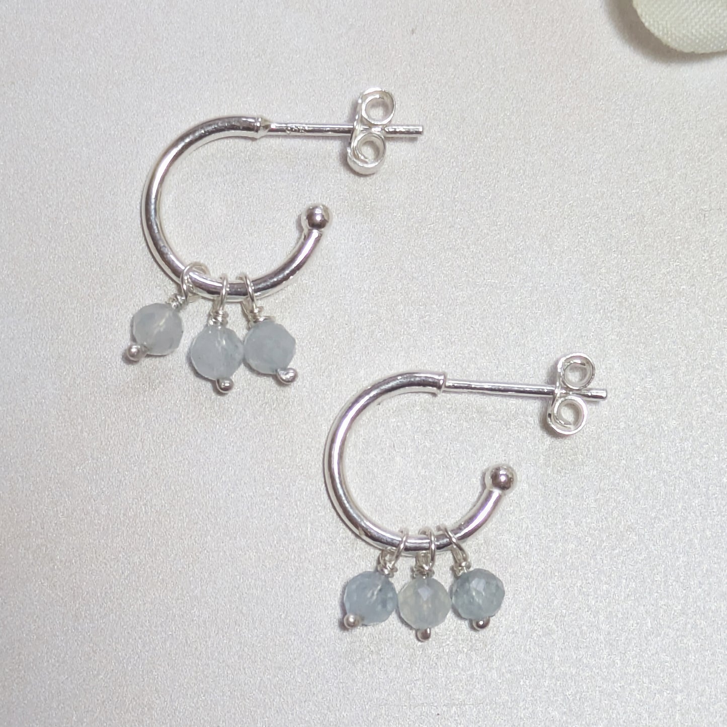 Silver hoop earrings with Aquamarine gemstone drops on a light grey background.