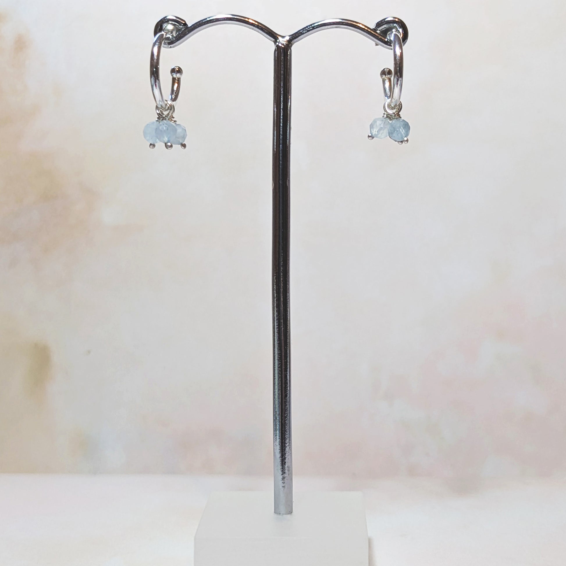 Pair of earrings with pale blue Aquamarine gemstones on a silver stand against a light background.