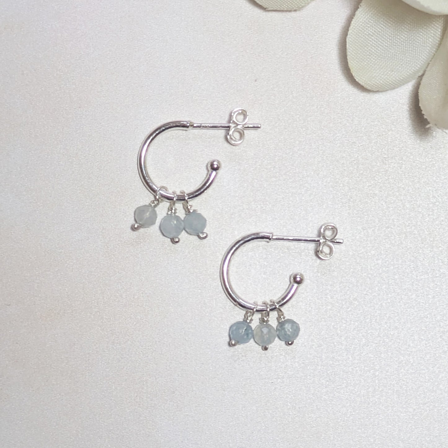 Silver hoop earrings with small round Aquamarine gemstones on a light background.