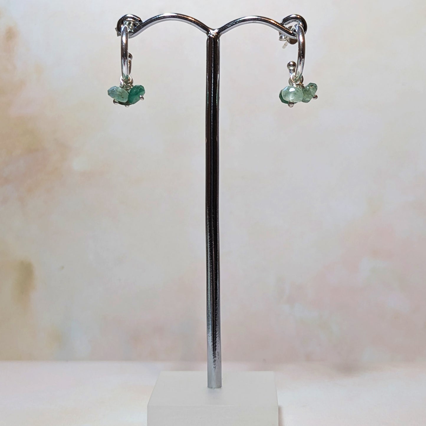 Emerald charm hoop earrings on a silver stand with a light background.