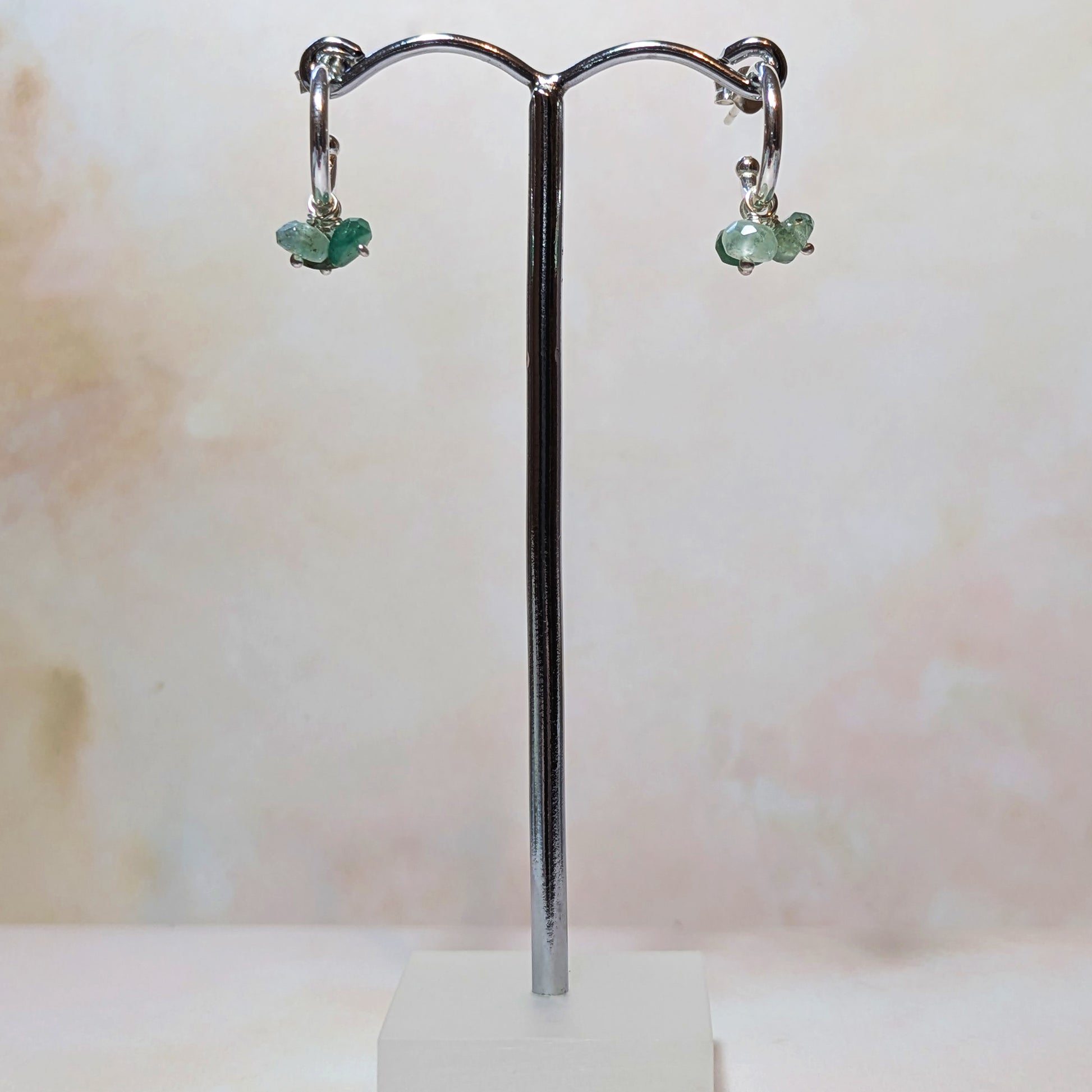 Emerald charm hoop earrings on a silver stand with a light background.