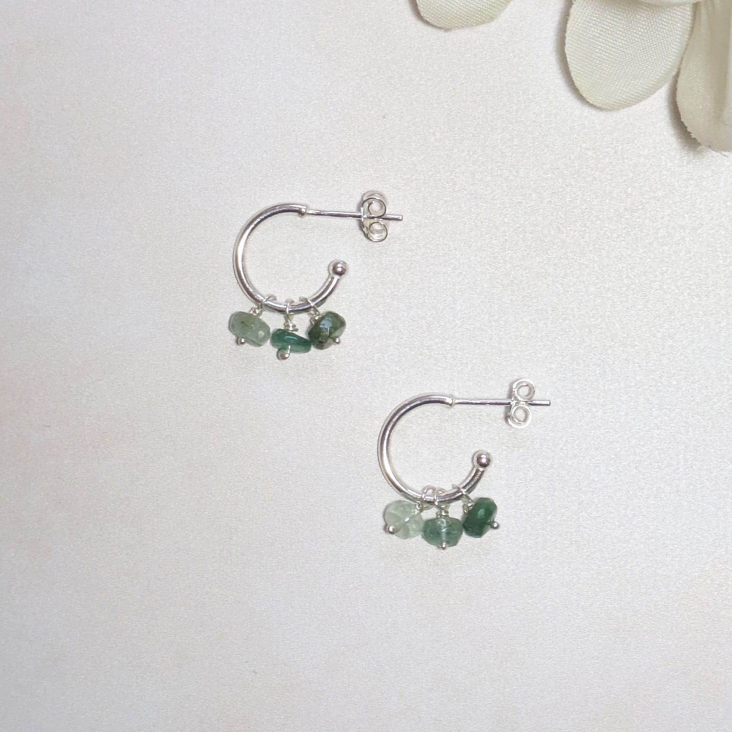 Silver hoop earrings with green Emerald gemstones on a white background.