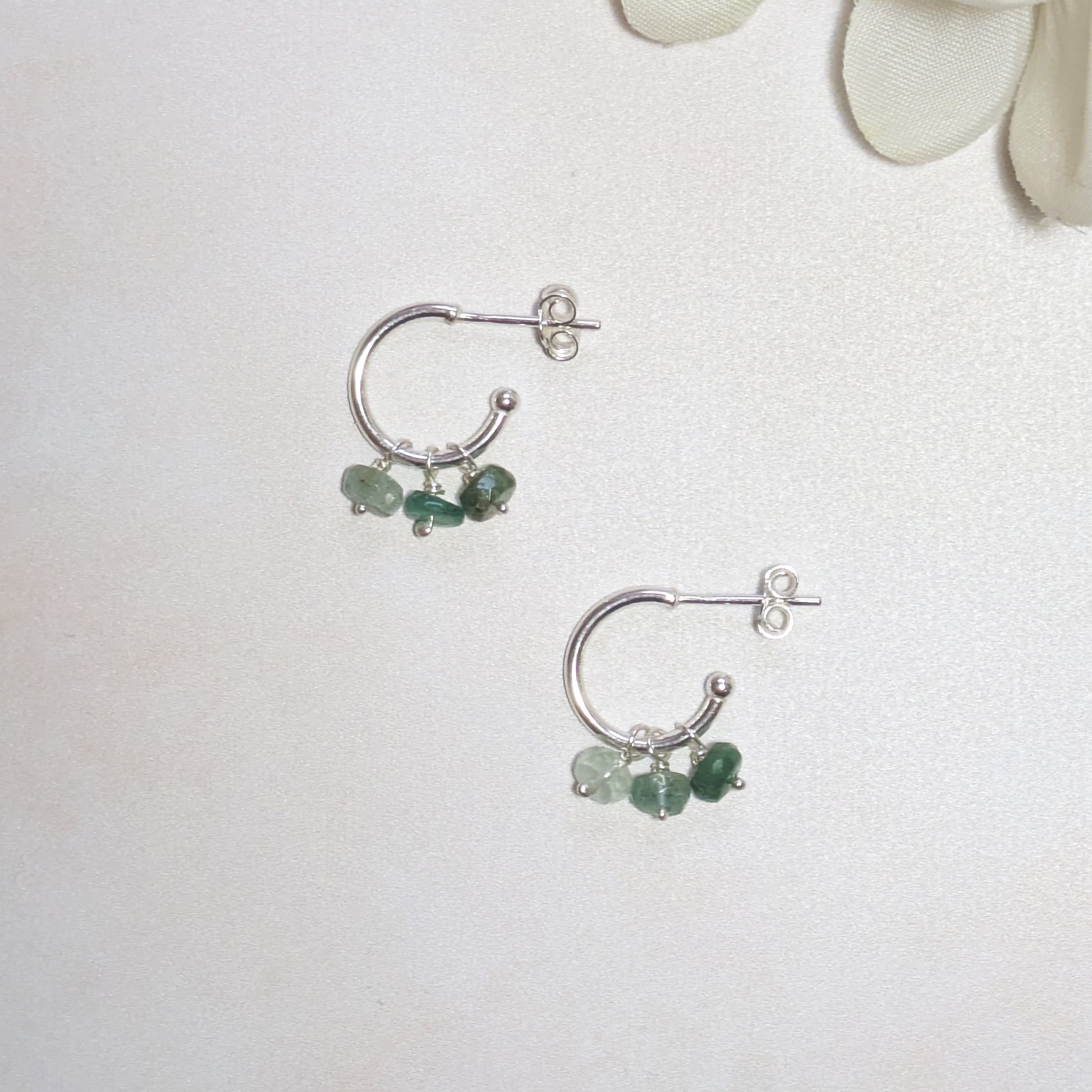 Silver hoop earrings with green Emerald gemstones on a white background.