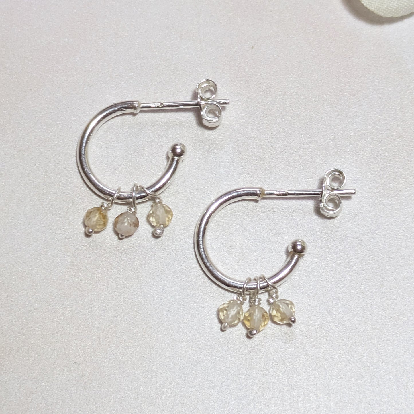 Silver hoop earrings with small yellow Citrine gemstones on a light background.