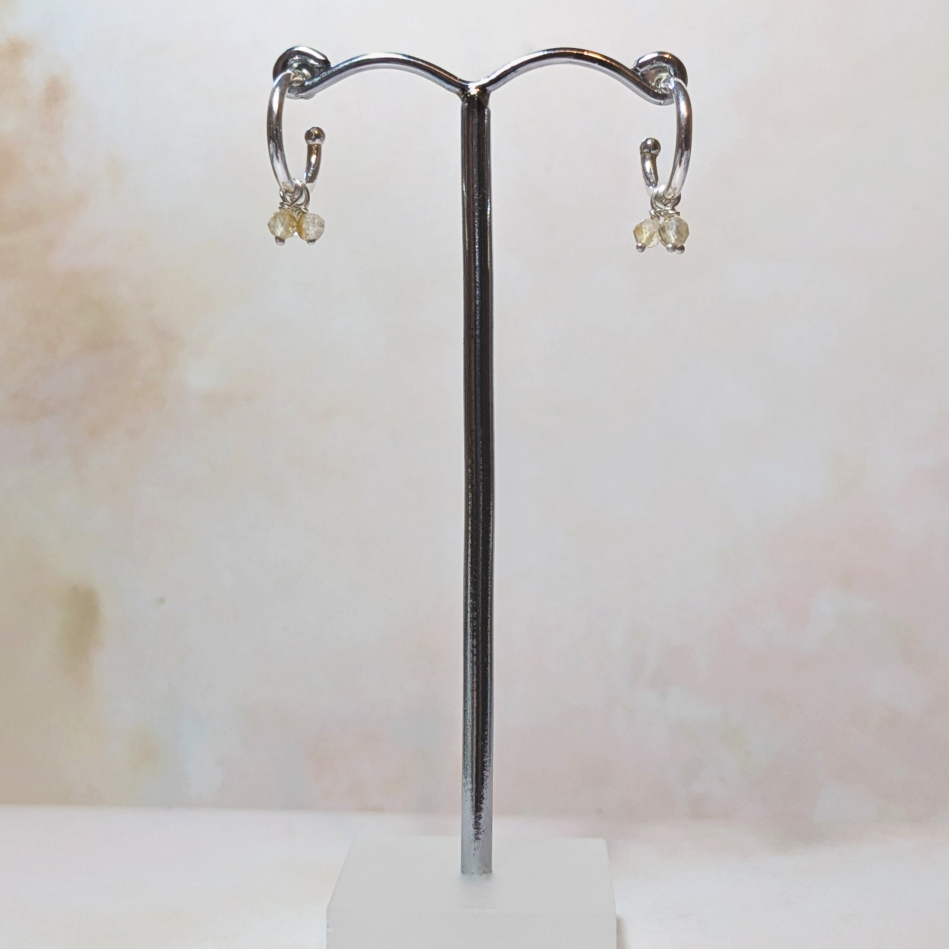 Silver hoop earrings with Citrines hanging from an earring stand on a light background.