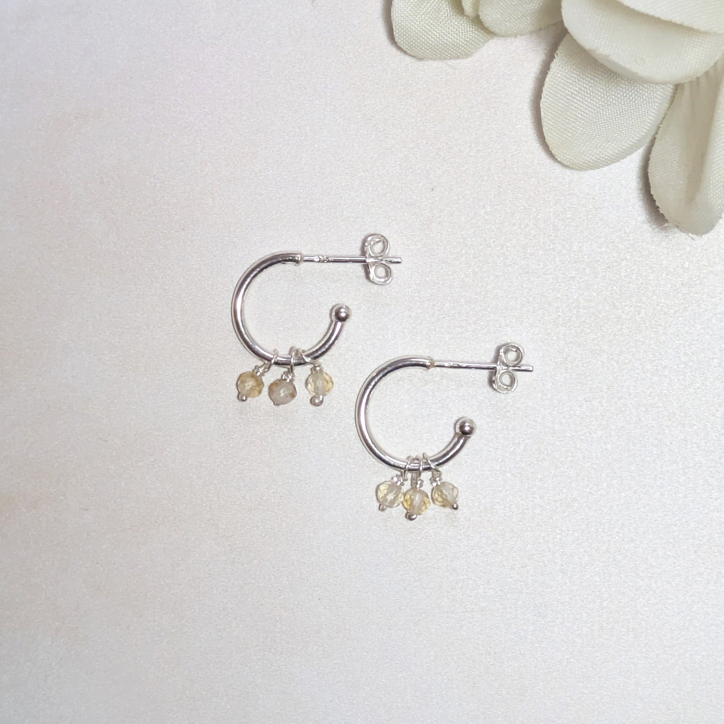 Silver hoop earrings with mini Citrine gemstones on a white background.