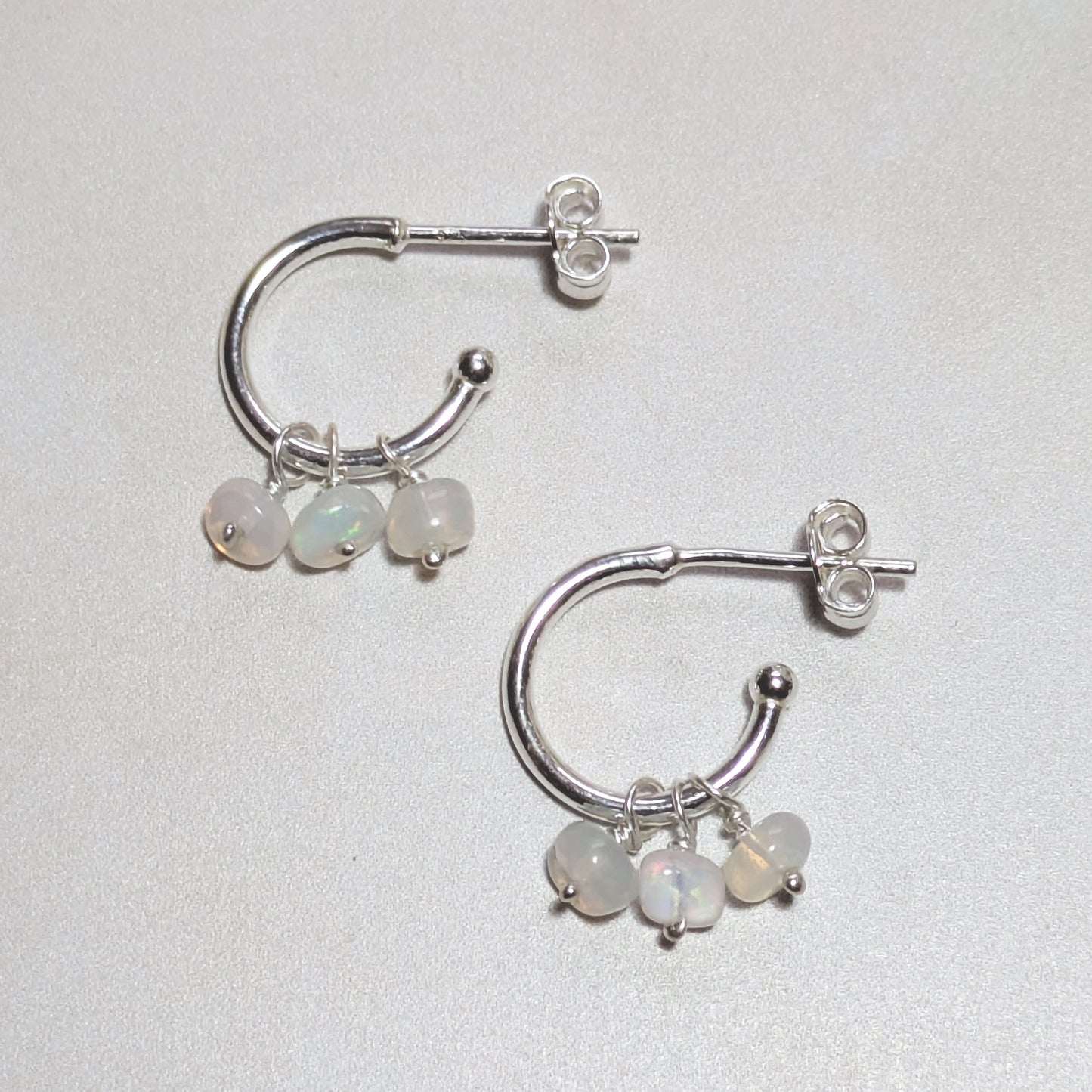Silver hoop earrings with small round Opal gemstone charms on a light grey background.
