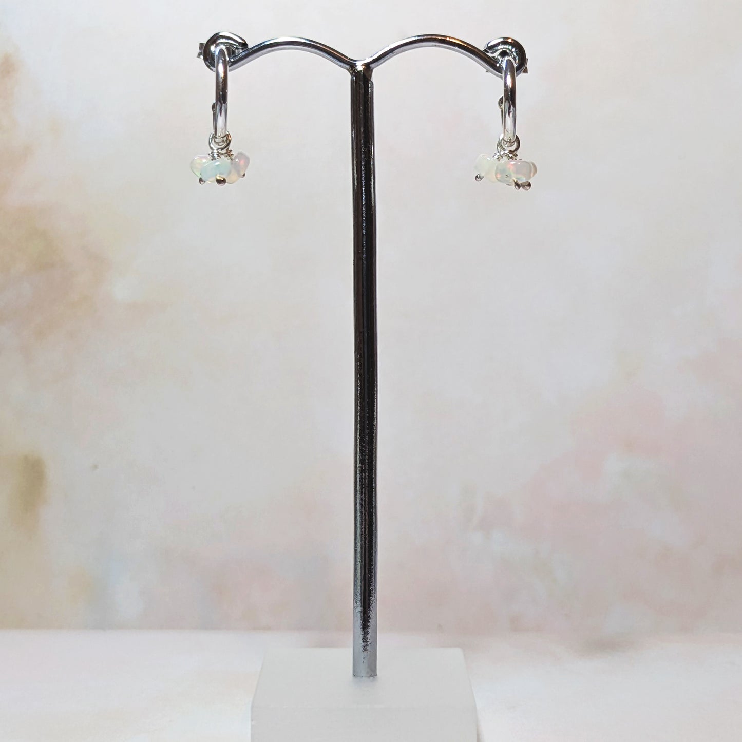 Silver hoop earrings with Opal gemstones on a stand against a soft neutral background.