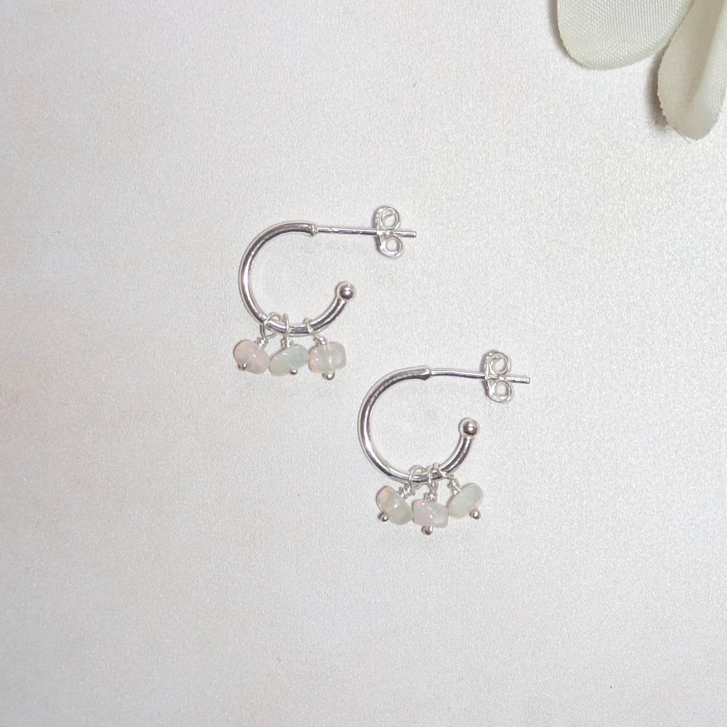 Silver hoop earrings with small Opal gemstones on a light background.