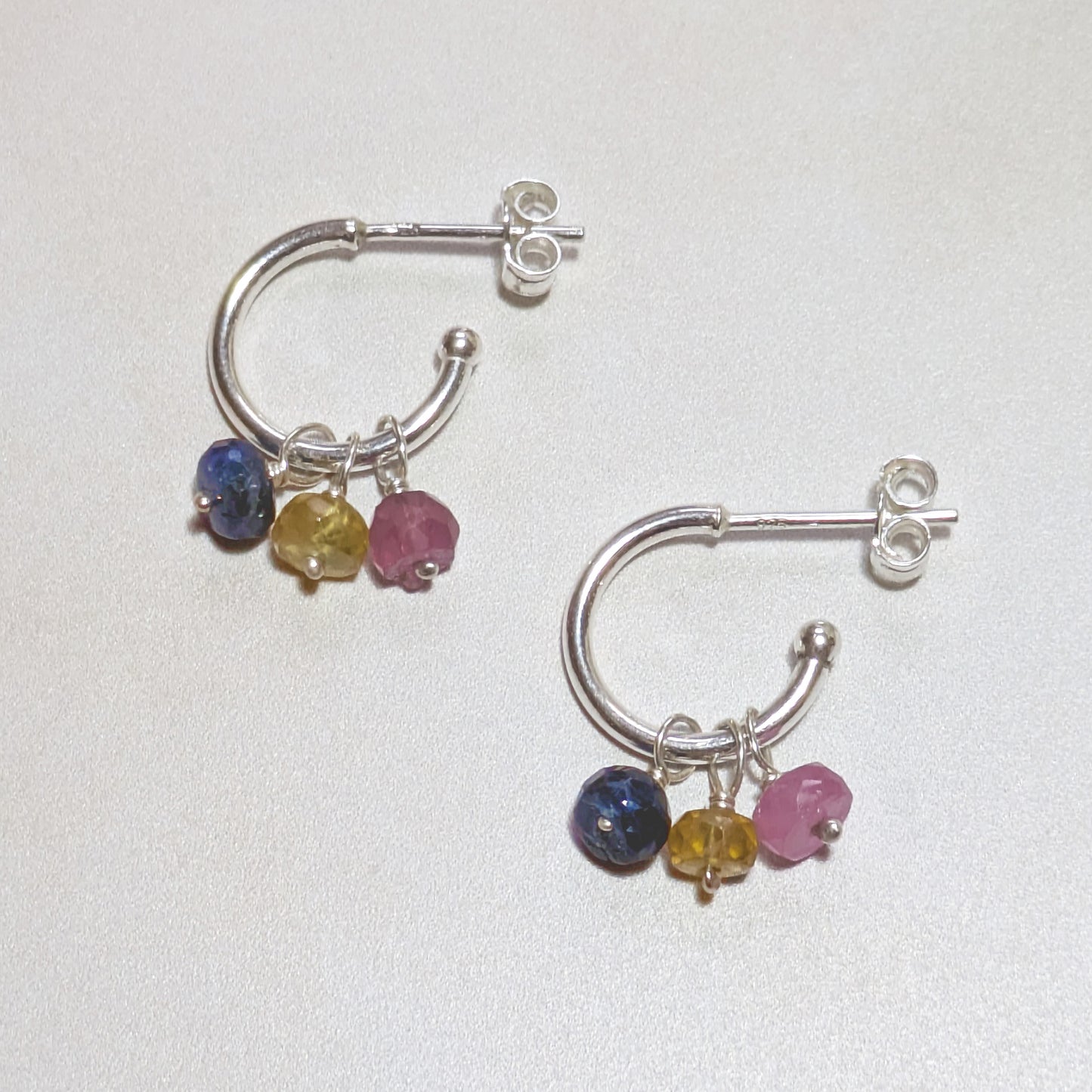 Silver hoop earrings with multicoloured Sapphire gemstones on a white background.