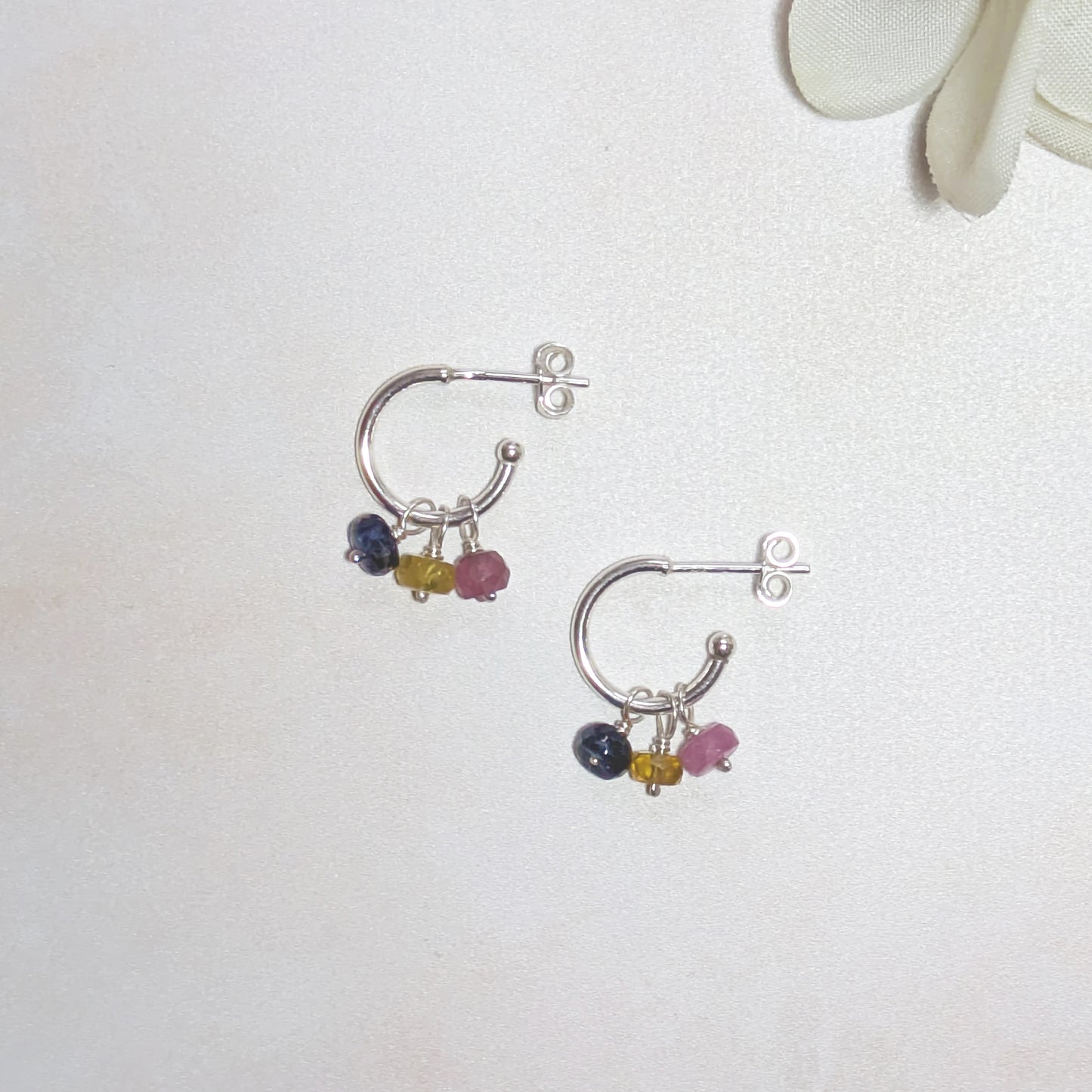 Silver hoop earrings with multicoloured Sapphire beads on a white background.