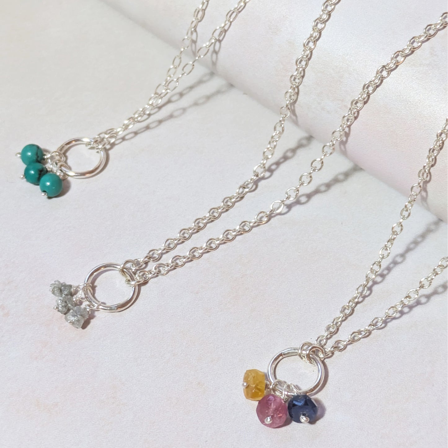 Three silver mini birthstone charm necklaces with gemstone pendants on a light background.