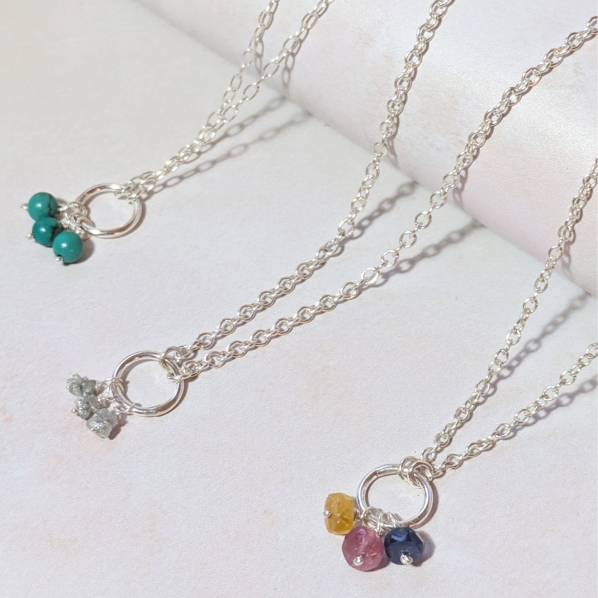 Three silver mini birthstone charm necklaces with gemstone pendants on a light background.