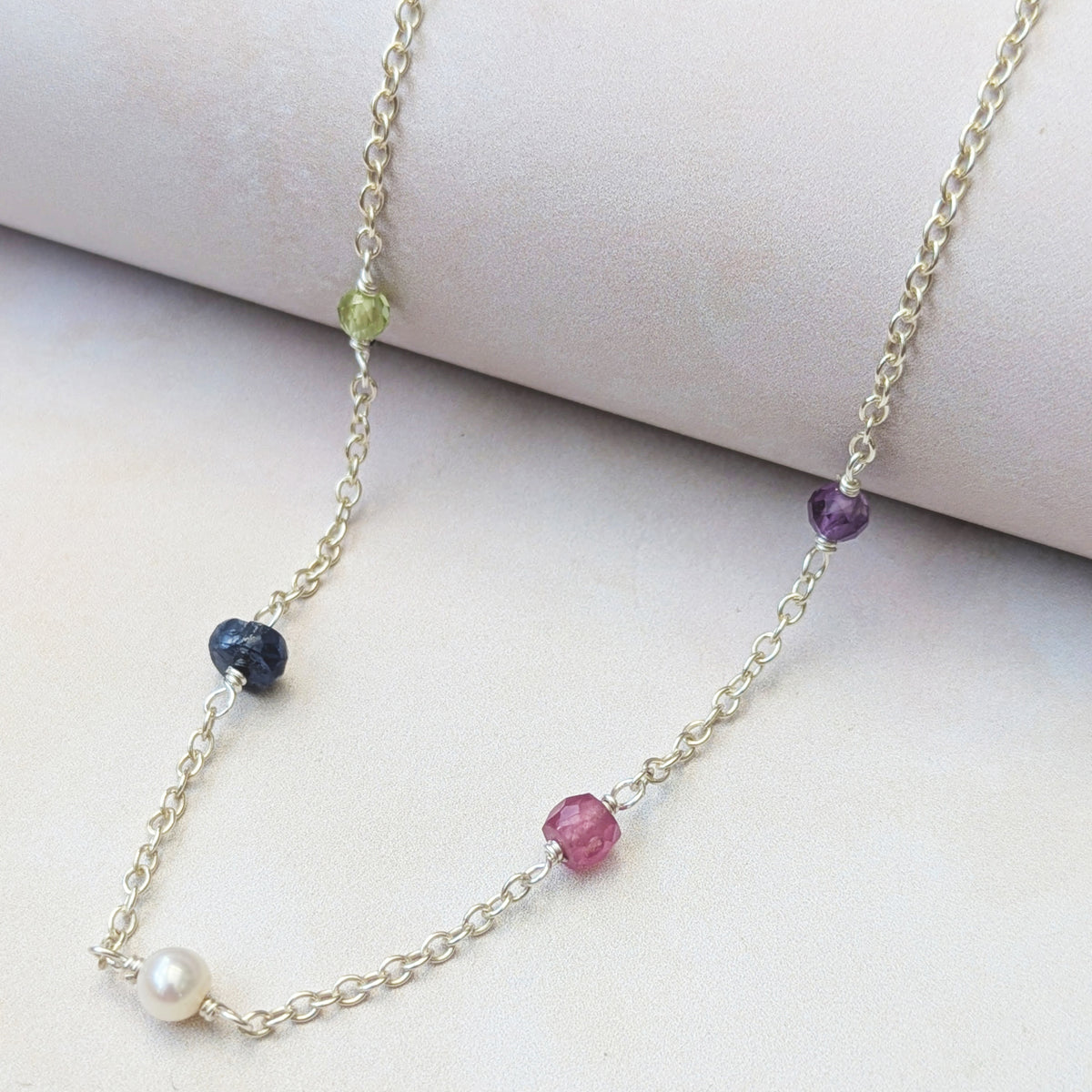 Lifestyle view of our personalised sterling silver family birthstone necklace  featuring natural ethically sourced gemstone beads shown on a neutral background.