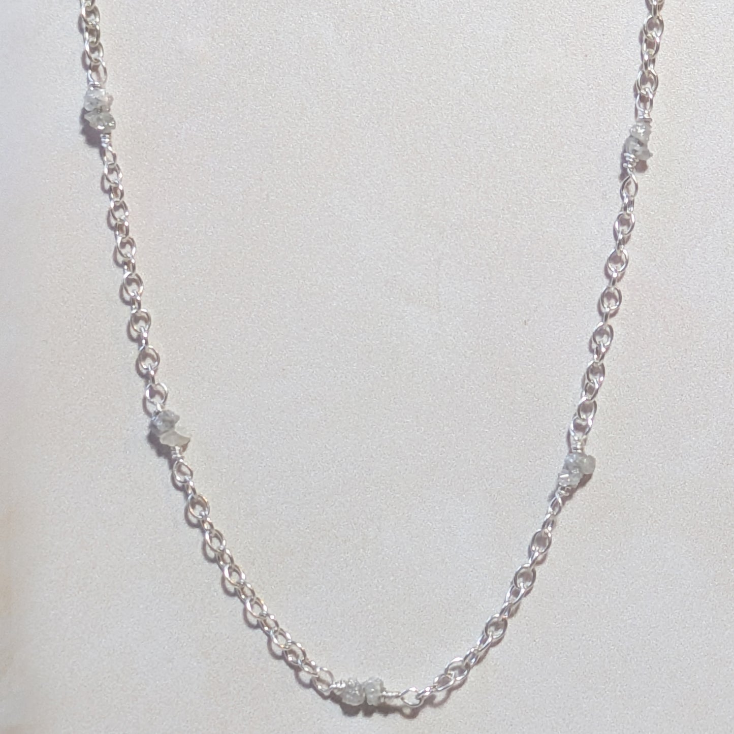 Silver chain necklace with stationed  rough diamond nuggets on a light grey background.