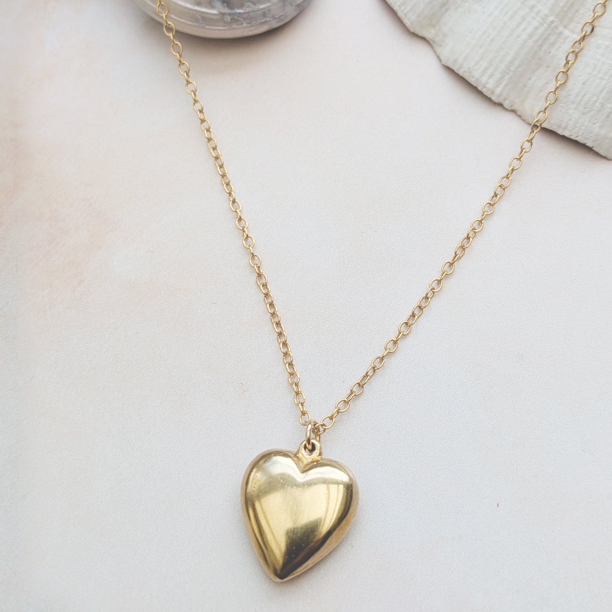 Gold heart necklace on a neutral background with shells