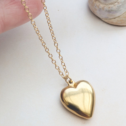 18ct Gold puffed heart necklace held in the hand, on a white background.