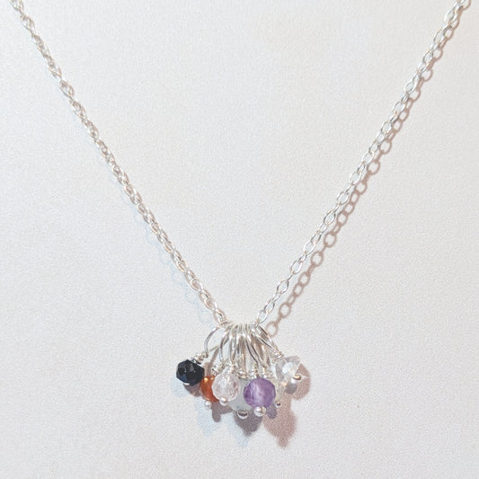Silver seven chakra charm necklace with small beads on a light background.