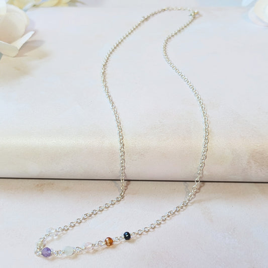 Silver seven chakra beaded necklace with gemstone beads on a light background.